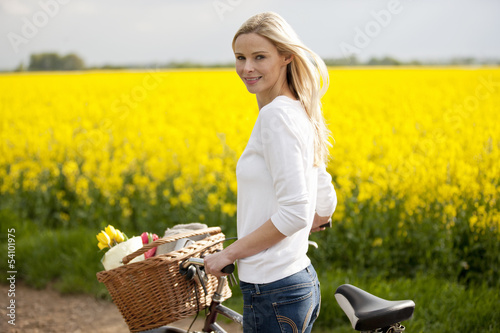 Photo: A young woman pushing a bicycle next to a rape seed field A young woman pushing a bicycle next to a rape seed field