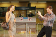 Photo: Businessman taking a picture of businesswoman using mobile phone, airline check-in attendant pointing at them Businessman taking a picture of businesswoman using mobile phone, airline check-in attendant pointing at them