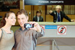 Photo: Businessman taking a picture using mobile phone, airline check-in attendant pointing at them Businessman taking a picture using mobile phone, airline check-in attendant pointing at them