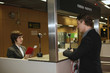 Photo: Airline check-in attendant checking businessman's passport at the airport check-in counter Airline check-in attendant checking businessman's passport at the airport check-in counter
