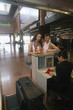 Photo: Airline check-in attendant checking passports of man and woman at the airport check-in counter Airline check-in attendant checking passports of man and woman at the airport check-in counter