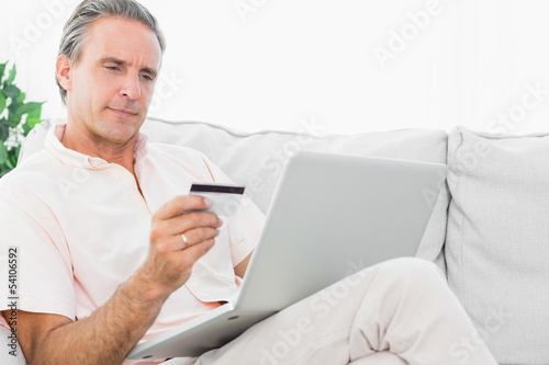 Photo: Man on his couch using laptop for online shopping Man on his couch using laptop for online shopping
