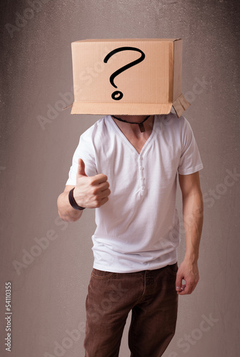 Photo: Young man gesturing with a cardboard box on his head with questi Young man gesturing with a cardboard box on his head with questi