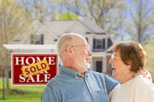 Photo: Senior Couple in Front of Sold Real Estate Sign and House Senior Couple in Front of Sold Real Estate Sign and House
