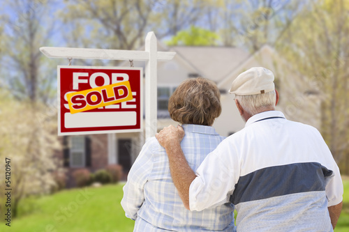 Photo: Senior Couple in Front of Sold Real Estate Sign and House Senior Couple in Front of Sold Real Estate Sign and House