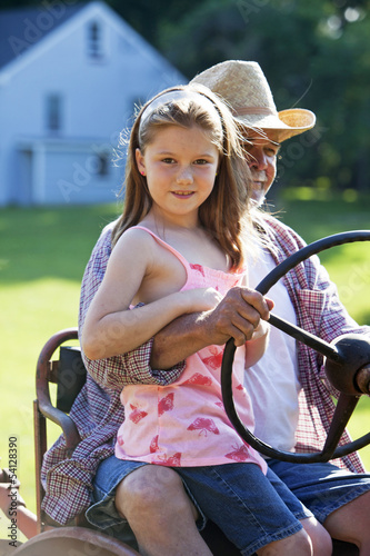 Photo: Young girl with grandfather driving a tractor on a farm Young girl with grandfather driving a tractor on a farm