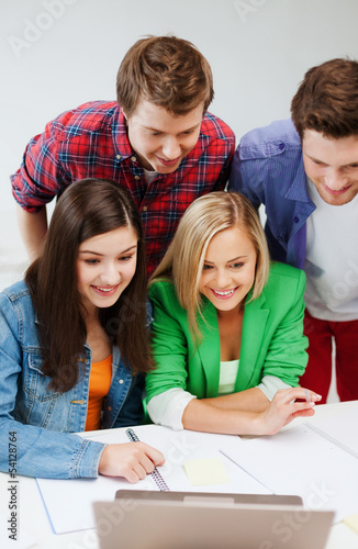 Photo: smiling students looking at laptop at school smiling students looking at laptop at school