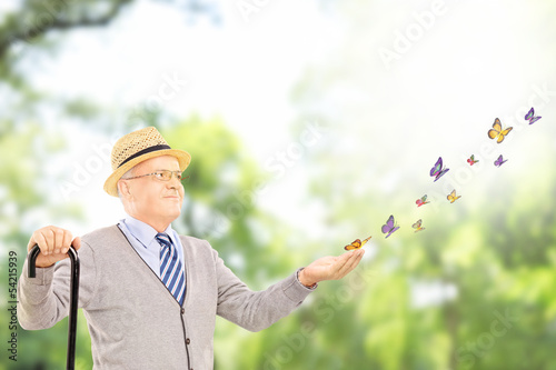 Photo: Mature smiling man holding a cane and looking at butterflies Mature smiling man holding a cane and looking at butterflies