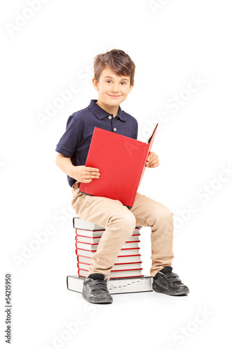 Photo: Smiling school boy sitting on a pile of books and reading Smiling school boy sitting on a pile of books and reading