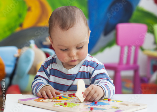 Photo: Toddler or a baby child playing with puzzle in a nursery. Toddler or a baby child playing with puzzle in a nursery.