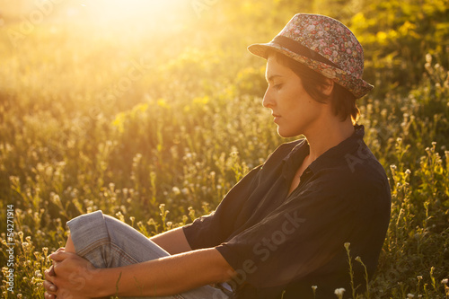 Photo: Cute girl sitting in the grass on a sunny evening Cute girl sitting in the grass on a sunny evening