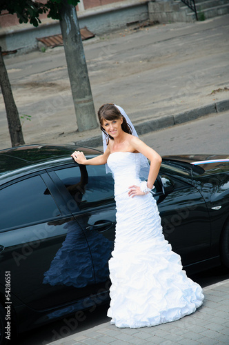 Photo: happy bride in white dress standing near wedding car happy bride in white dress standing near wedding car