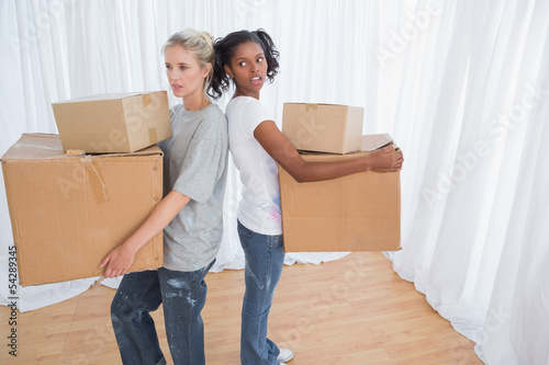 Photo: Friends standing back to back holding moving boxes Friends standing back to back holding moving boxes