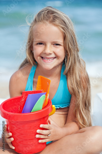 Photo: Little girl on the beach with small bucket and shovels for sand Little girl on the beach with small bucket and shovels for sand