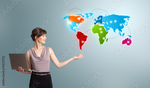 Photo: Young woman holding a laptop and presenting colorful world map Young woman holding a laptop and presenting colorful world map