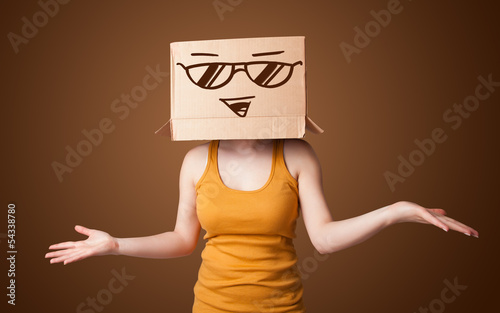 Photo: Young lady gesturing with a cardboard box on her head with smile Young lady gesturing with a cardboard box on her head with smile