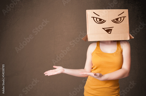 Photo: Young woman gesturing with a cardboard box on her head with evil Young woman gesturing with a cardboard box on her head with evil
