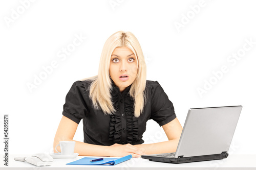 Photo: Surpised blond woman sitting on a table in her office Surpised blond woman sitting on a table in her office