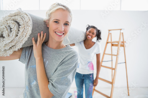 Photo: Happy housemates carrying rolled up rug in new home Happy housemates carrying rolled up rug in new home