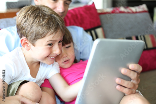 Photo: Father and children playing with tablet at home Father and children playing with tablet at home