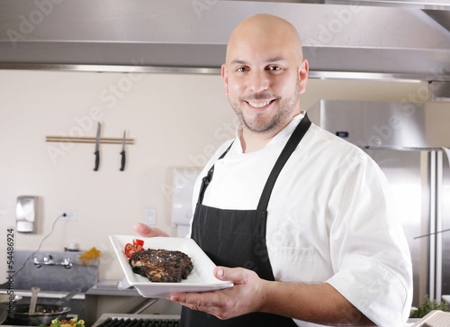 Photo: young male chef presenting a juicy ribeye steak with tomatoes young male chef presenting a juicy ribeye steak with tomatoes