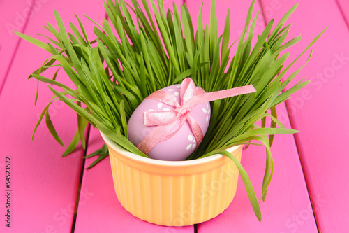 Photo: Easter egg in bowl with grass on pink wooden table close up Easter egg in bowl with grass on pink wooden table close up