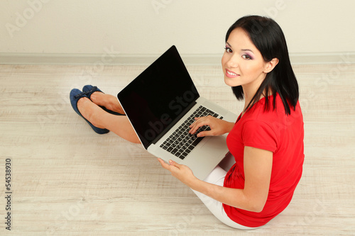 Photo: Beautiful young woman sitting with notebook in room Beautiful young woman sitting with notebook in room