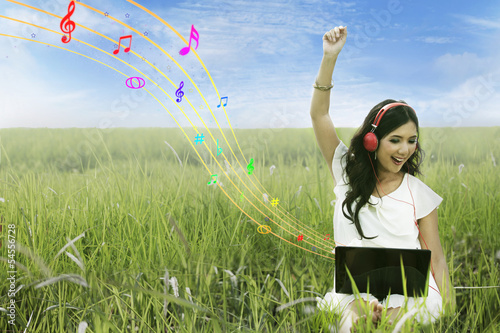Photo: Attractive female listening to music on green field Attractive female listening to music on green field