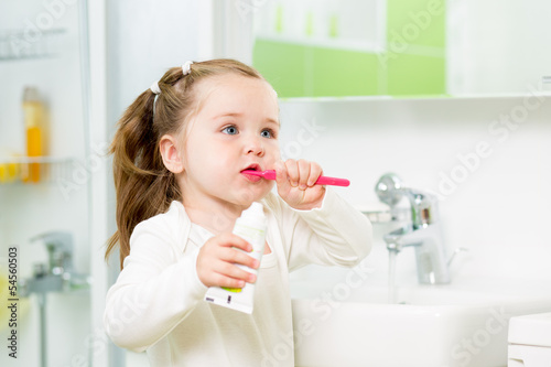 Photo: Child girl brushing teeth in bathroom Child girl brushing teeth in bathroom