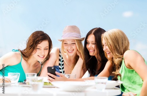 Photo: girls looking at smartphone in cafe on the beach girls looking at smartphone in cafe on the beach