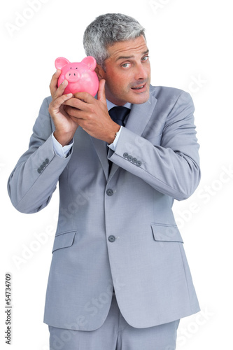 Photo: Curious businessman holding piggy bank Curious businessman holding piggy bank