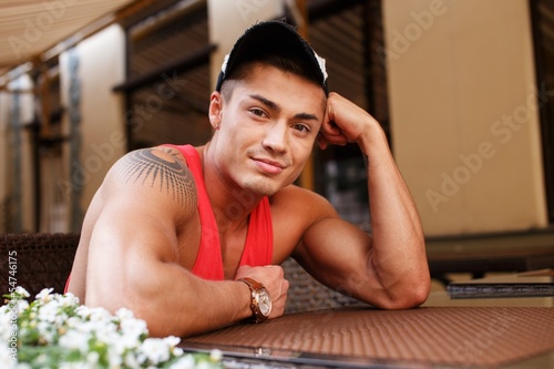 Photo: Stylish young man in cap sitting behind table Stylish young man in cap sitting behind table