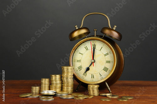 Photo: Antique clock and coins on wooden table on black background Antique clock and coins on wooden table on black background