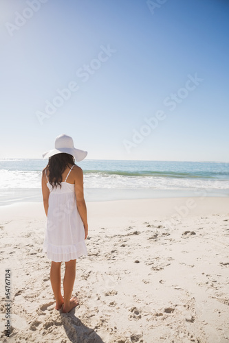 Photo: Brunette in white sunhat and dress looking at the ocean Brunette in white sunhat and dress looking at the ocean