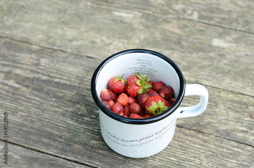 Photo: Wild strawberry in metal cup on wooden table Wild strawberry in metal cup on wooden table