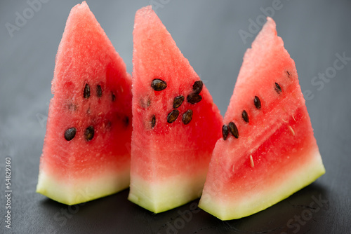 Photo: Segments of juicy watermelon on black wooden background Segments of juicy watermelon on black wooden background
