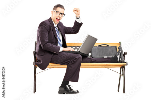 Photo: Excited young businessman with a laptop sitting on a bench Excited young businessman with a laptop sitting on a bench