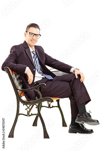 Photo: Smiling young man in a suit sitting on a bench Smiling young man in a suit sitting on a bench