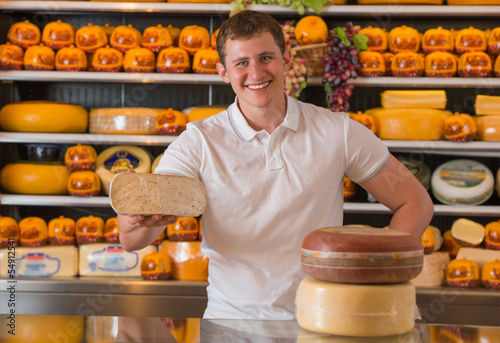 Photo: Handsome male owner of a cheese store standing with cheese piece Handsome male owner of a cheese store standing with cheese piece