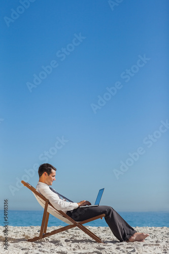 Photo: Young businessman on his deck chair using his laptop Young businessman on his deck chair using his laptop
