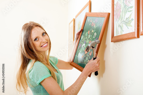 Photo: Happy blonde woman hanging picture with flowers Happy blonde woman hanging picture with flowers