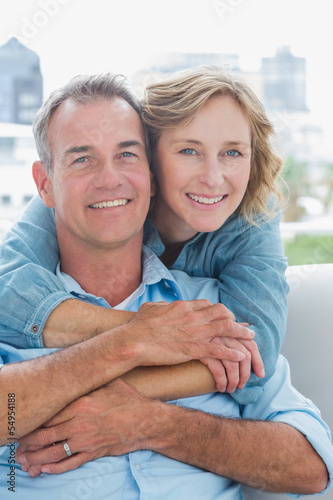 Photo: Happy woman hugging her husband on the couch from behind Happy woman hugging her husband on the couch from behind