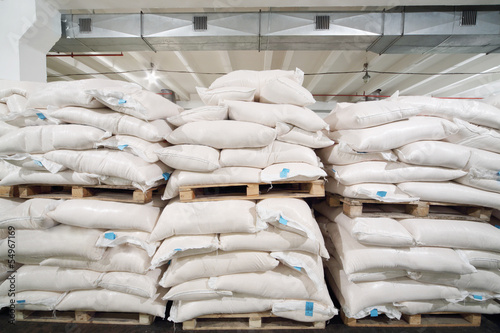 Photo: Rows of big white sacks at large warehouse in modern factory. Rows of big white sacks at large warehouse in modern factory.