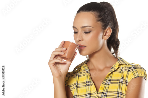 Photo: young brunette enjoys the smell of her coffee from the machine young brunette enjoys the smell of her coffee from the machine