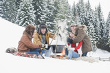 Foto: Österreich, Land Salzburg, Flachau, Junge Männer und Frauen sitzen im Schnee am Kamin Österreich, Land Salzburg, Flachau, Junge Männer und Frauen sitzen im Schnee am Kamin