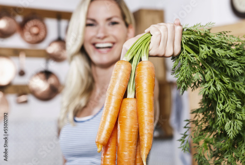 Photo: Italien, Toskana, Magliano, Junge Frau, die Karotten in Küche hält, Lächeln Italien, Toskana, Magliano, Junge Frau, die Karotten in Küche hält, Lächeln