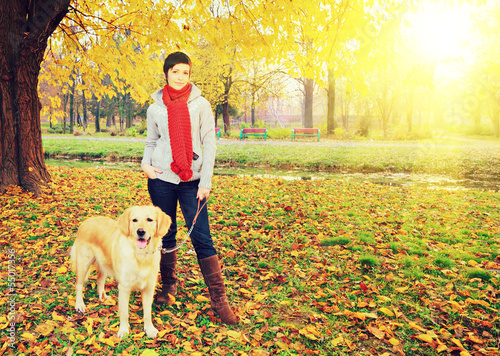 Photo: Young female and her dog posing in autumn in a park Young female and her dog posing in autumn in a park