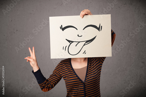Photo: Woman holding a paper with cute smiley face on it in front of he Woman holding a paper with cute smiley face on it in front of he
