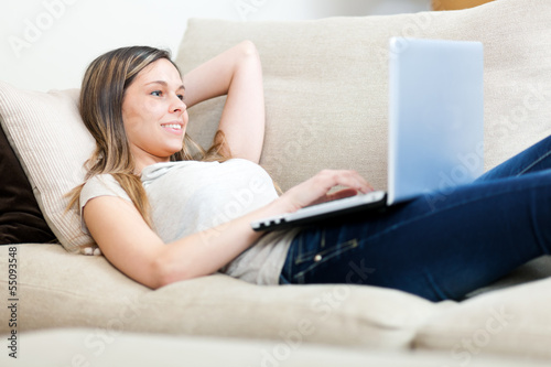 Photo: Young woman relaxing on the sofa with her laptop Young woman relaxing on the sofa with her laptop