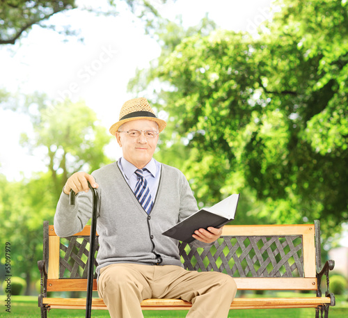 Photo: Senior man sitting on a wooden bench and reading a book Senior man sitting on a wooden bench and reading a book